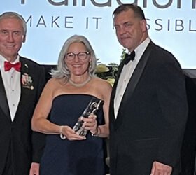 Two hosts present the Global Impact award to recipient on a stage in front of an audience.